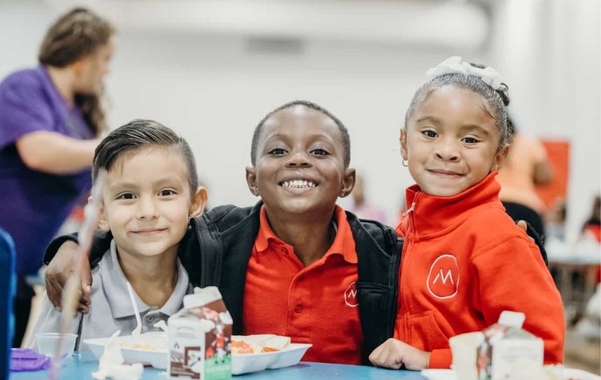 Three kids at lunch smiling towards camera