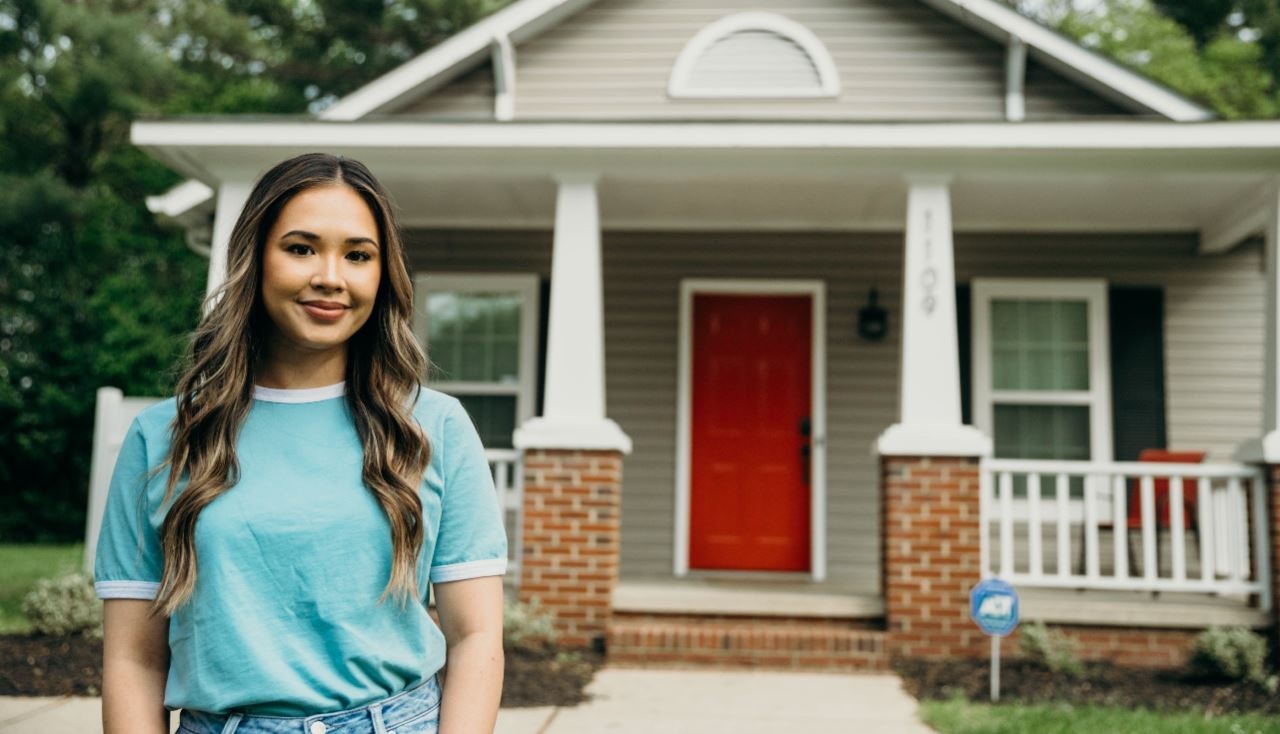 Woman with long hair and blue shirt standing in front of a house